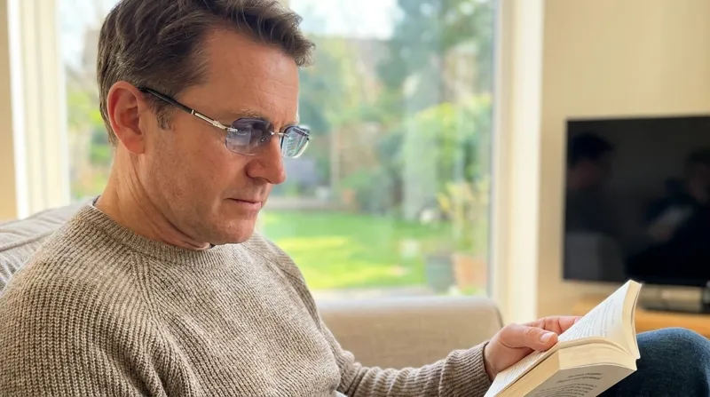 Man reading a book on the sofa wearing BlueLume glasses, brand photo